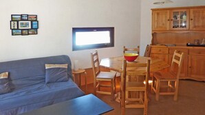 A living room with a blue sofa, a wooden dining table with chairs, a TV mounted on the wall, and wooden cabinets in the background. - 119 LE Sunny Snow 1650 (LES ORRES 1650)