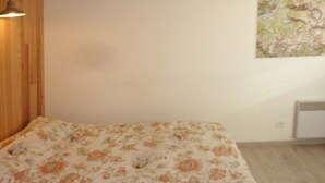 A bedroom with a floral bedspread, a wooden headboard, a wall-mounted lamp, and a small painting. - D204 LES CEMBROS 1650 (LES ORRES 1650)