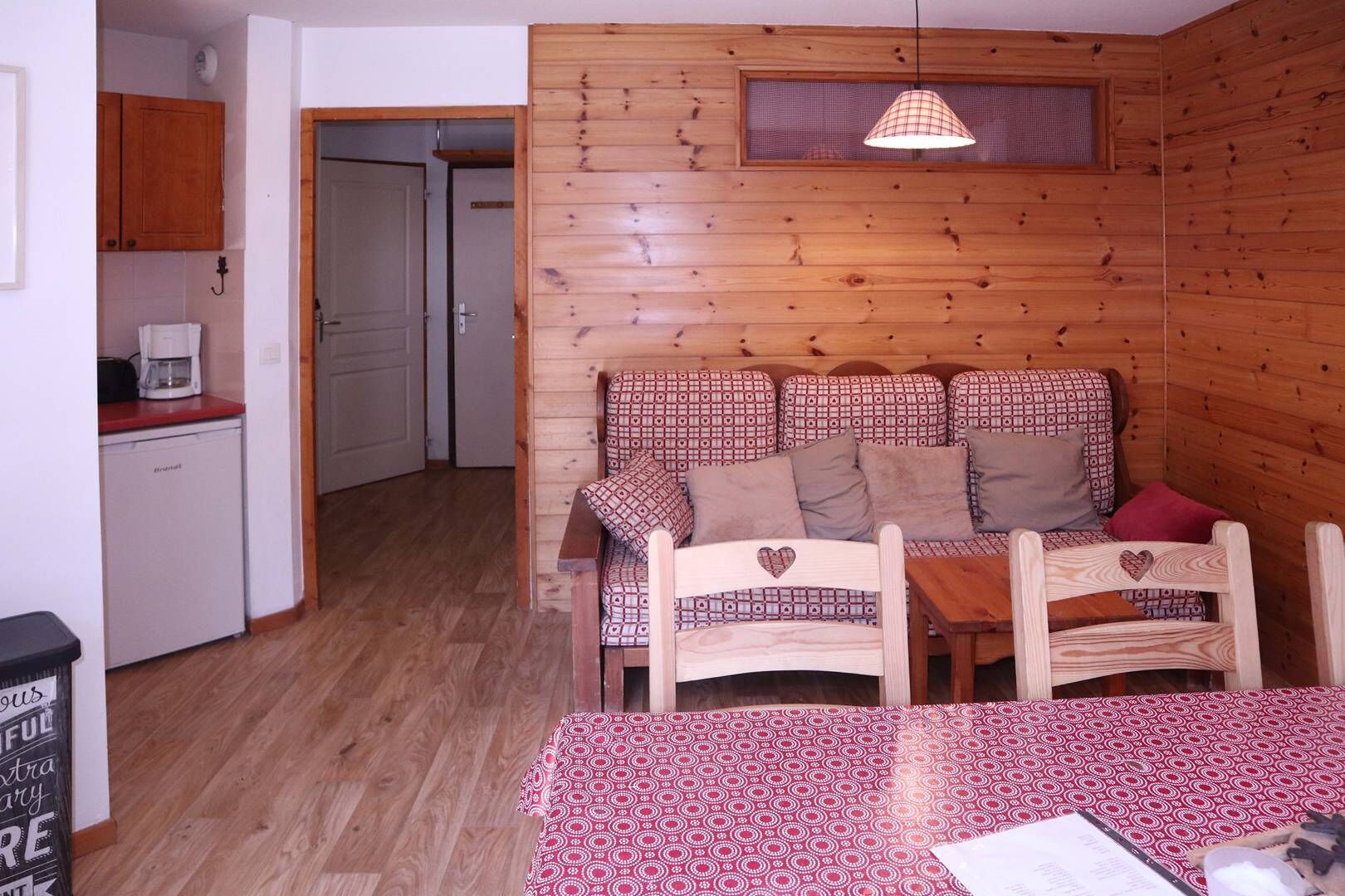 A cozy cabin-style room with a wooden interior, a sofa with patterned cushions, a small dining table, and a kitchenette area.