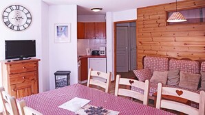 Una habitación acogedora con una mesa de madera, sillas, un televisor, una zona de cocina y un sofá estampado.