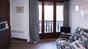 A room with a wooden floor, a sofa with patterned upholstery, a television, and a radiator.