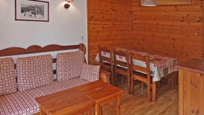 A cozy room with a wooden sofa, a dining table with chairs, and a small kitchen area. - 2222 LES Silenes 1800 (LES ORRES 1800)