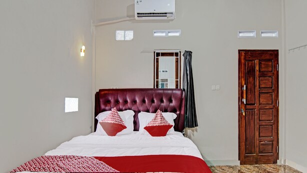 A bedroom with a large bed, a wooden door, and an air conditioning unit. - Hotel O Elisa Hill (Pangkalan Kerinci)