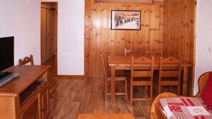 A wooden-paneled room with a dining table, chairs, a bed with a patterned blanket, and a television on a wooden cabinet.