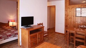 A room with a bed, a wooden TV stand with a TV, a desk, and a chair.