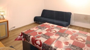 Et lille rum med en sofa, et bord med et tæppe, en lampe og et ur på væggen.