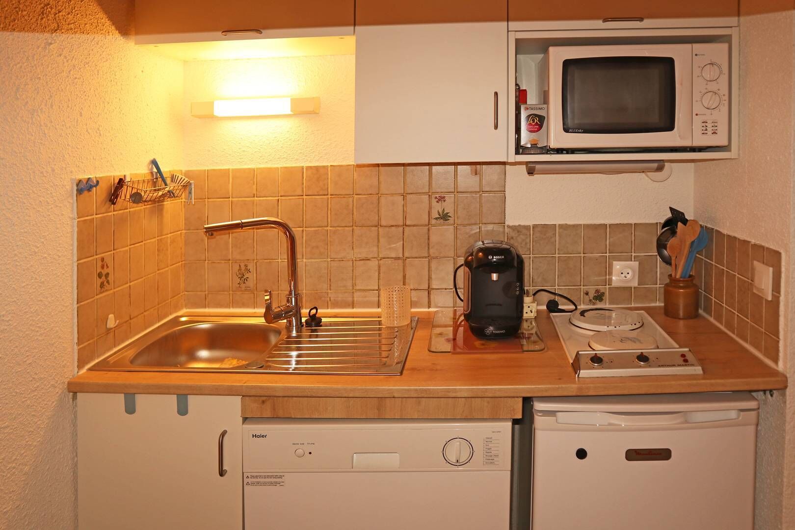 A compact kitchen with a sink, a Bosch coffee maker, a microwave, and a dishwasher.