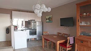 A modern kitchen with white cabinets, a built-in oven, and a stainless steel refrigerator. There is a dining table with four chairs and a wooden cabinet with glassware. - 130 LE Sunny Snow 1650 (LES ORRES 1650)