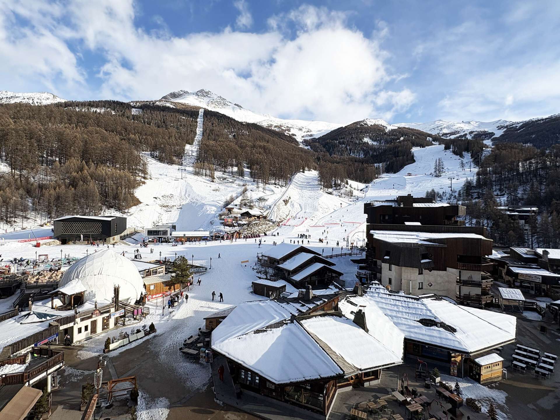 A snow-covered ski resort with buildings, a ski lift, and a mountain backdrop.