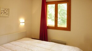 A bedroom with a bed, a window with a red curtain, a wall-mounted light, and a radiator. - N°101 Balcon des Airelles (LES ORRES 1800)