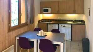 A compact kitchen with wooden cabinets, a microwave, a dishwasher, and a dining table with purple chairs. - N°101 Balcon des Airelles (LES ORRES 1800)