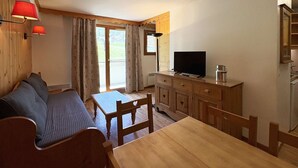 Un área de estar acogedora con un sofá, una mesa de comedor de madera y un televisor.