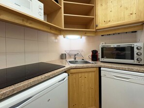 Eine kompakte Küche mit einer schwarzen Induktionskochplatte, einem eingebauten Geschirrspüler, einer Mikrowelle und Holzschränken.