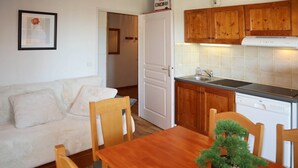 Un espace de vie compact comprenant une table à manger en bois, des chaises, un canapé blanc et un coin cuisine avec des meubles en bois et un lave-vaisselle.