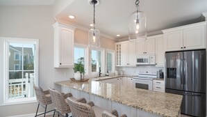 A kitchen with white cabinets, a stainless steel refrigerator, and a granite countertop. - Hobbs Realty - “Carolina Pearl” | New! Inlet Views & Private Heatable Pool (Holden Beach)