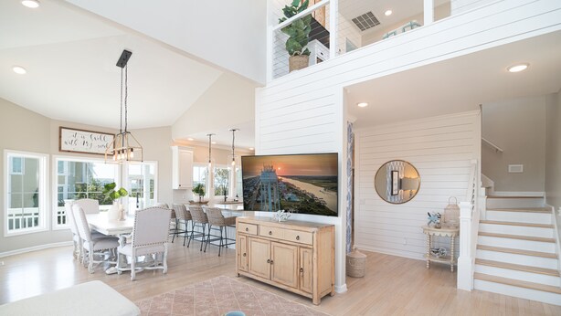 A spacious living room with a high ceiling, a dining area, and a staircase leading to an upper level. - Hobbs Realty - “Carolina Pearl” | New! Inlet Views & Private Heatable Pool (Holden Beach)