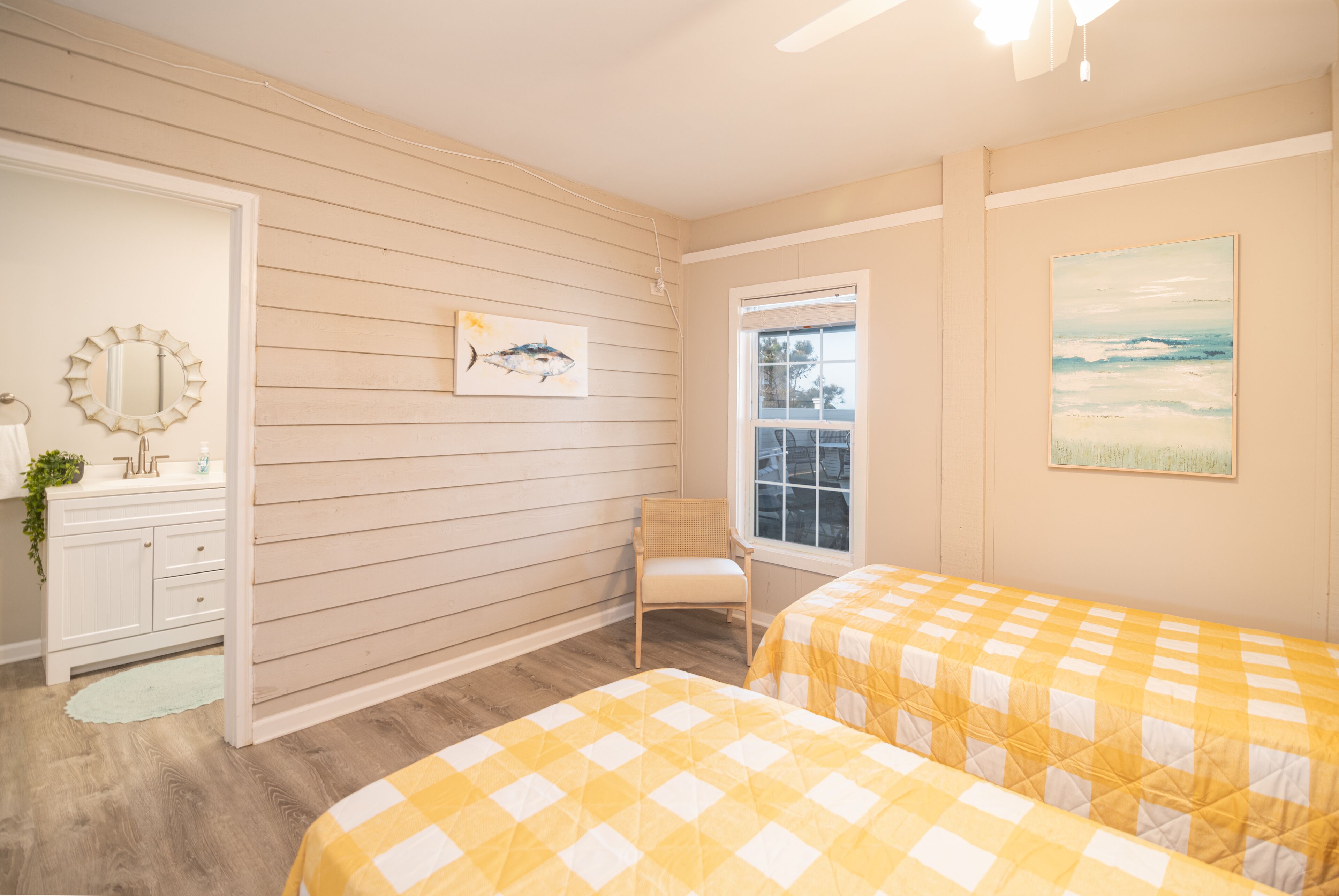 A bedroom with two beds, a dresser, a chair, a window, and artwork on the walls.
