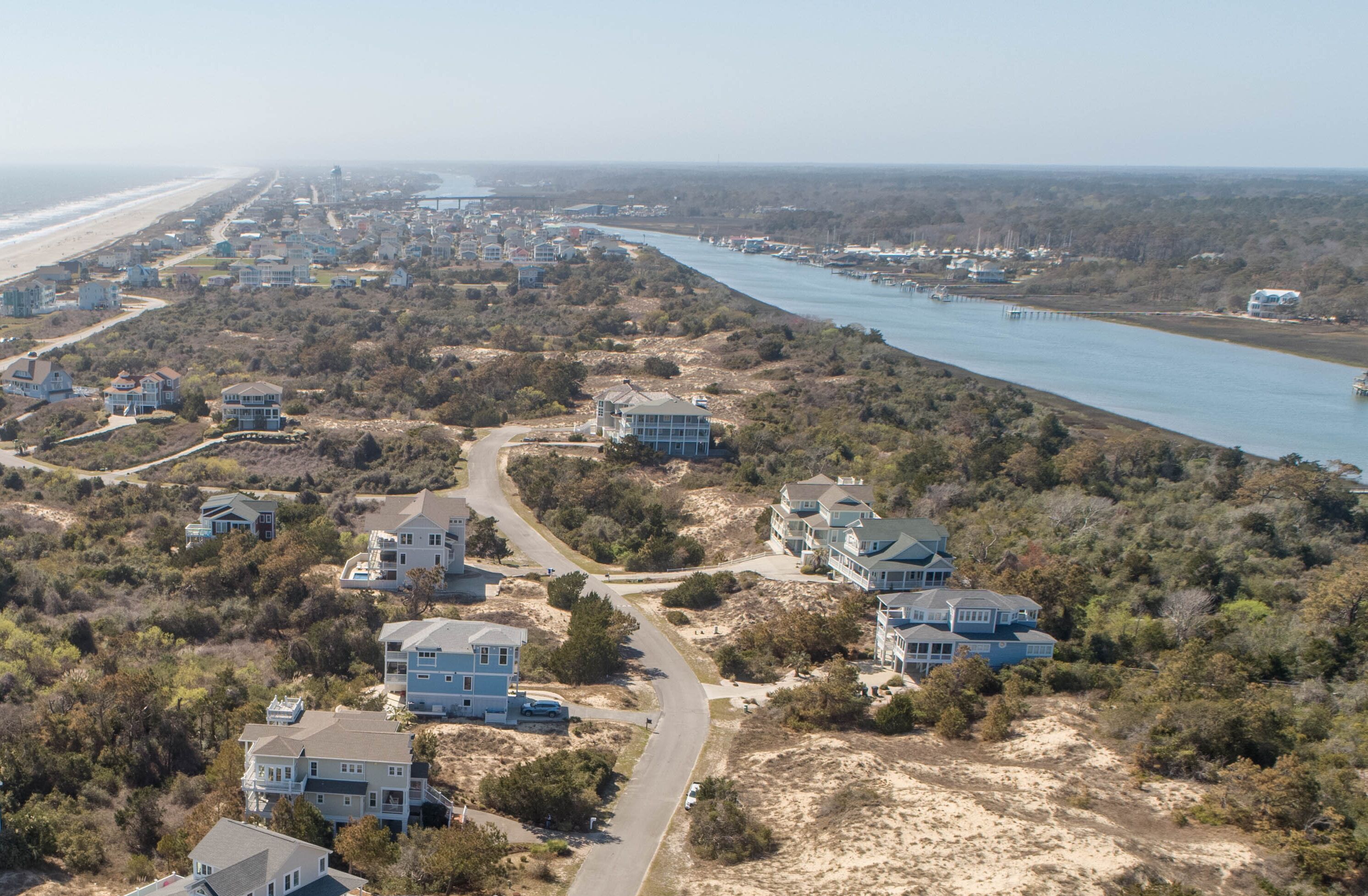 Un quartier résidentiel situé sur la côte, avec des maisons le long d’une rivière, un pont et une plage en arrière-plan.
