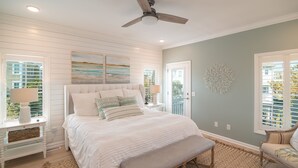 A bedroom with a large bed, a bench, a ceiling fan, and artwork on the walls. - Hobbs Realty - “Carolina Pearl” | New! Inlet Views & Private Heatable Pool (Holden Beach)