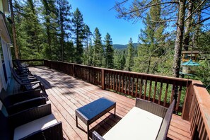 Une terrasse en bois, agrémentée de mobilier d’extérieur, entourée d’arbres et offrant une vue sur un ciel dégagé.
