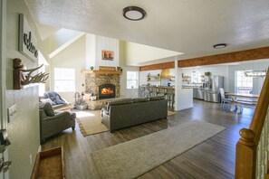 A spacious living room with a fireplace, a dining area, and a kitchen. - Sleeps 18 · 4 Private Acres · Canyon Views & Arcade (Cloudcroft)