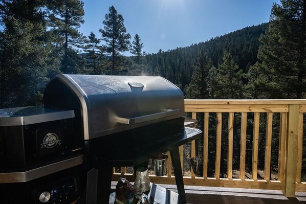 A barbecue grill on a wooden deck with a forested mountain background. - Sleeps 18 · 4 Private Acres · Canyon Views & Arcade (Cloudcroft)