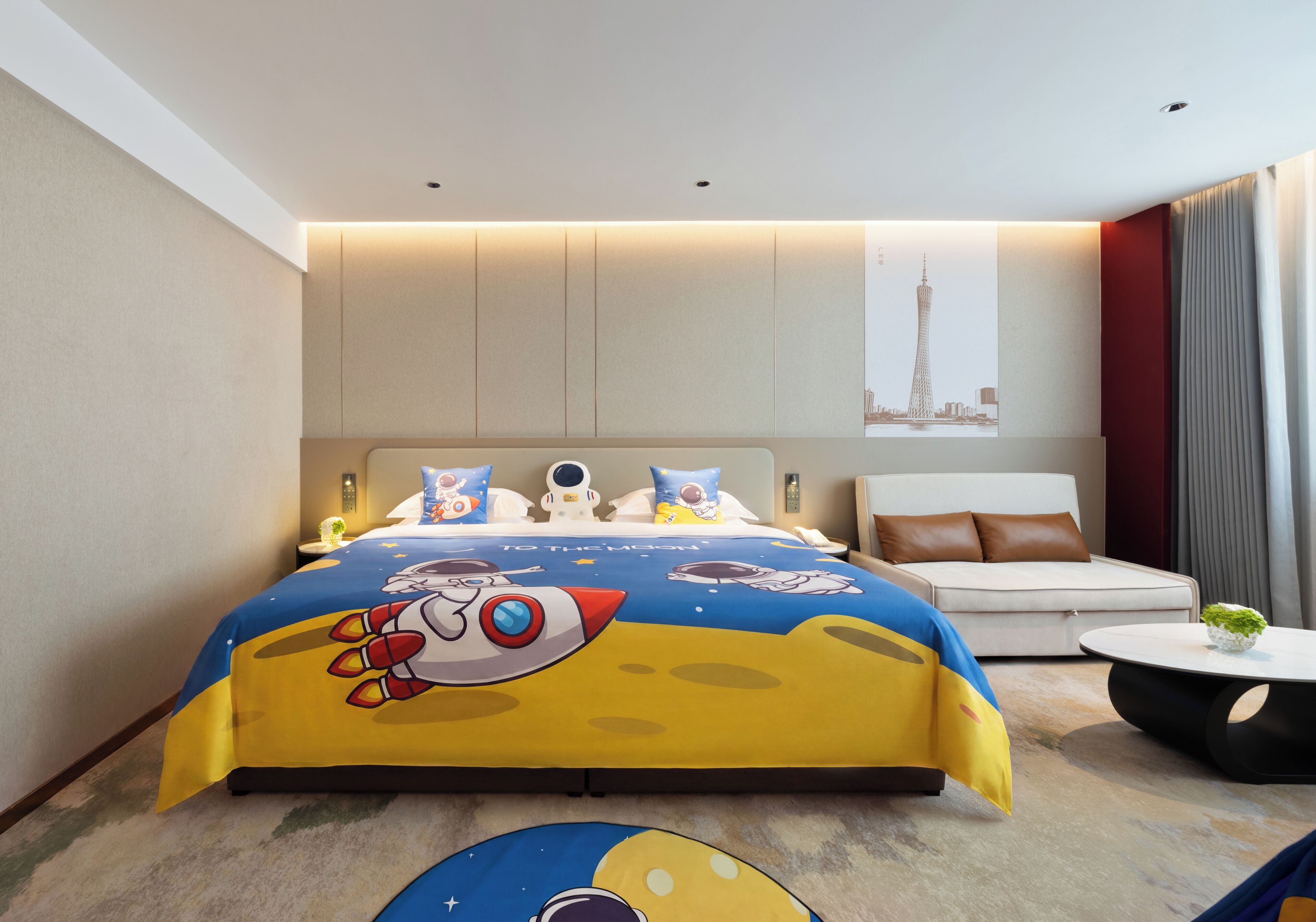 A modern hotel room with a large bed, a sofa, a small round table, and a cityscape artwork on the wall.