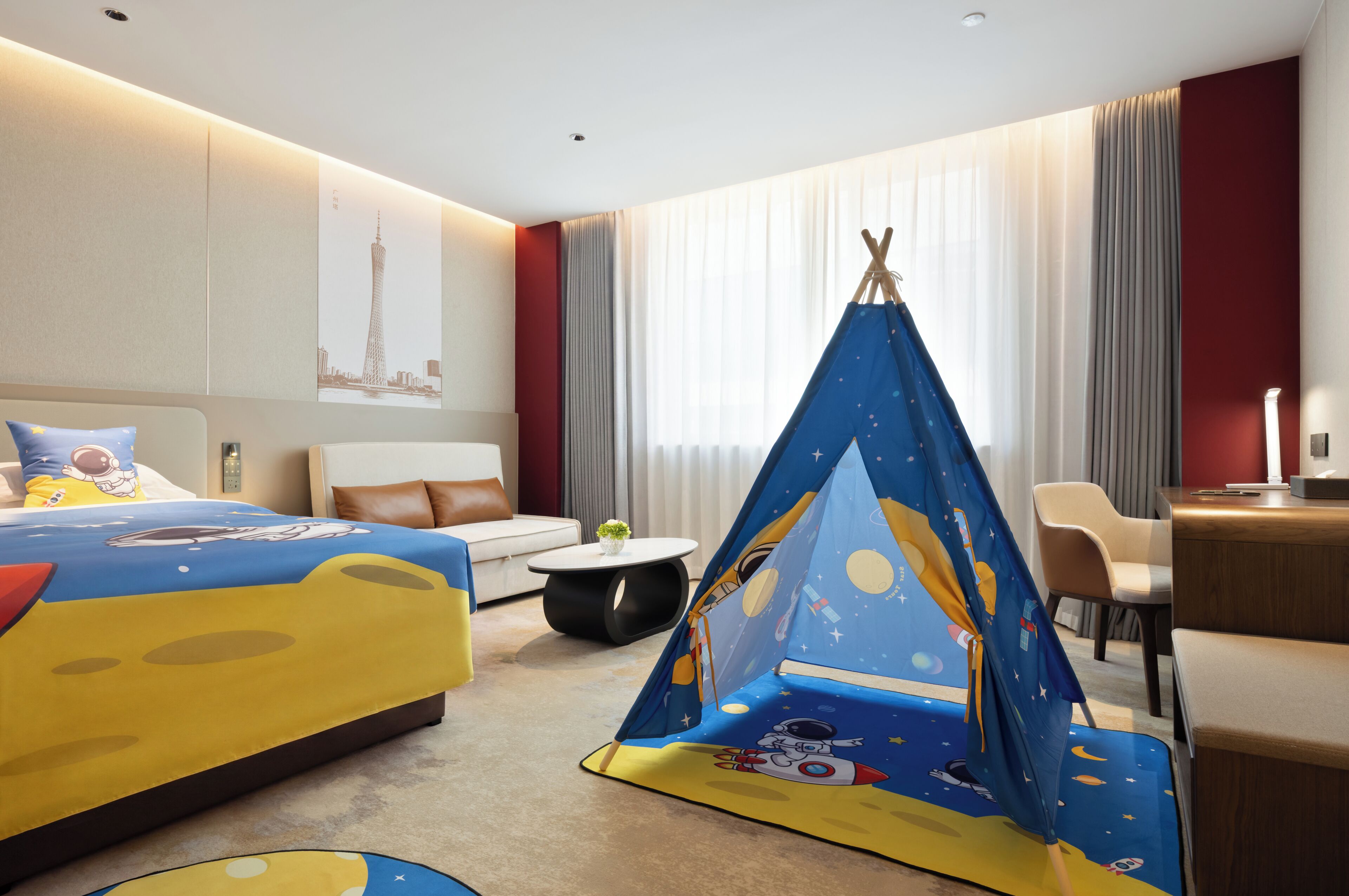 Quarto de hotel com cama, sofá, escrivaninha, cadeira, mesinha e uma tenda com tema espacial.