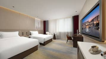 Een hotelkamer met twee bedden, een bureau, een stoel, een televisie en een bijzettafeltje met een kop en een lepel.