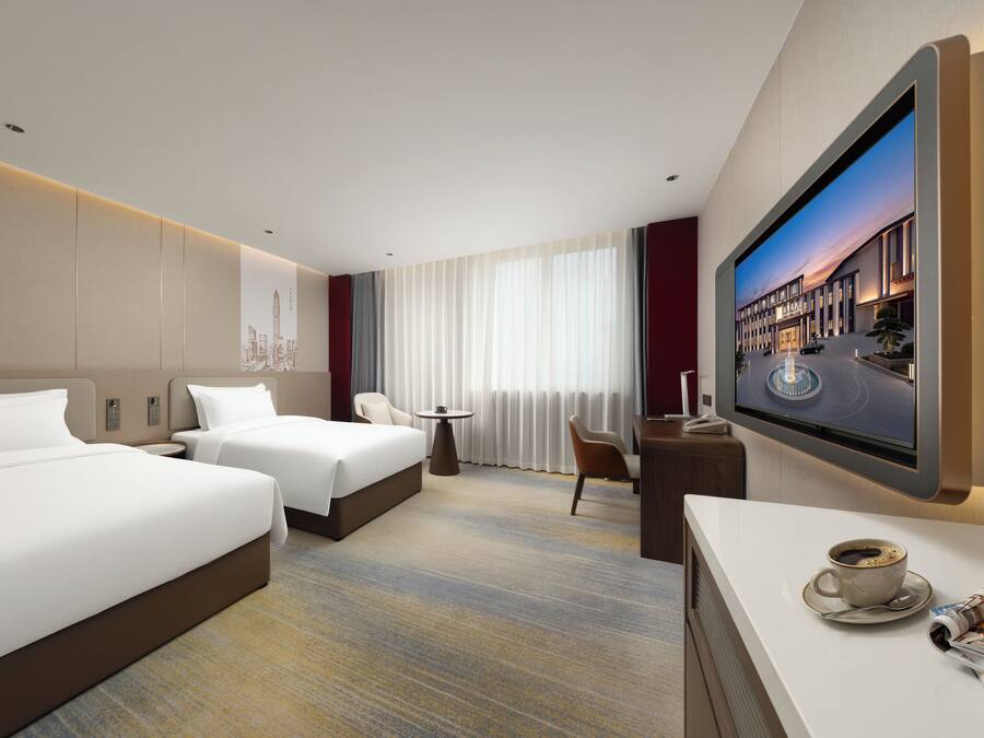A hotel room with two beds, a desk, a chair, a television, and a coffee table with a cup and a spoon.