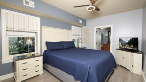 Une chambre à coucher comprenant un lit, une table de chevet, une commode, un ventilateur de plafond et un téléviseur.