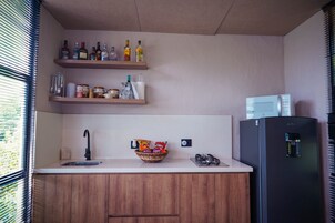 A modern kitchen with wooden cabinets, a black refrigerator, a microwave, and shelves with bottles and jars.