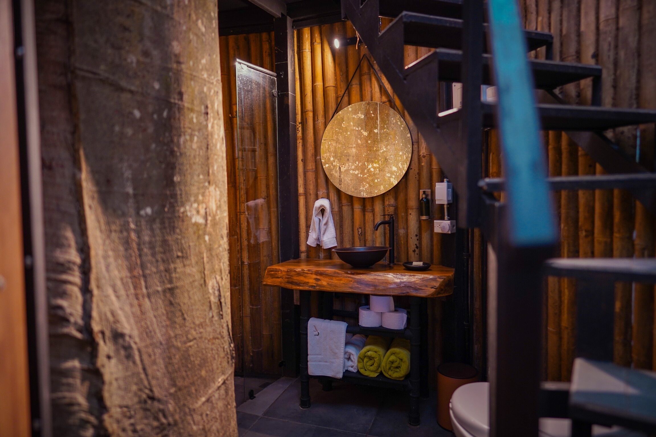 A rustic bathroom with a wooden vanity, a round mirror, and a toilet.