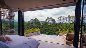 A bedroom with a large bed, a view of a lush forest, and a small outdoor hot tub. - Amanatu Ecolodge & Spa  (Quimbaya)