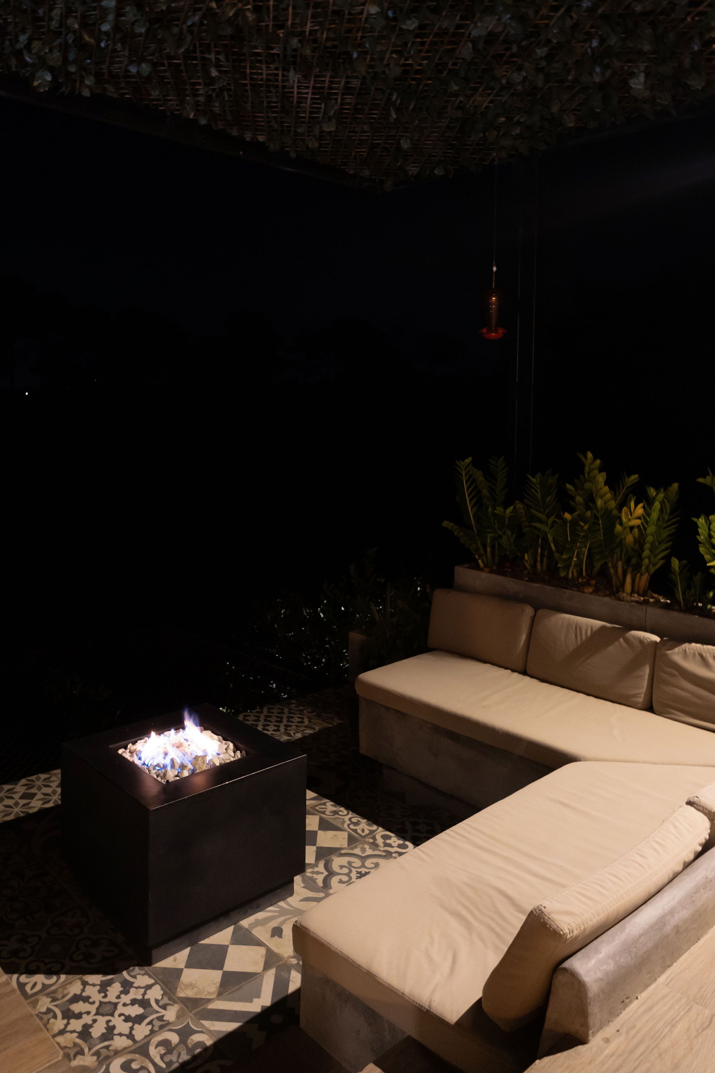 A dark outdoor seating area with a fire pit, a sofa, and potted plants.