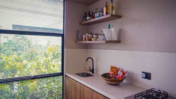 Una cocina con ventana, un lavamanos, una estufa a gas y repisas con botellas y frascos.