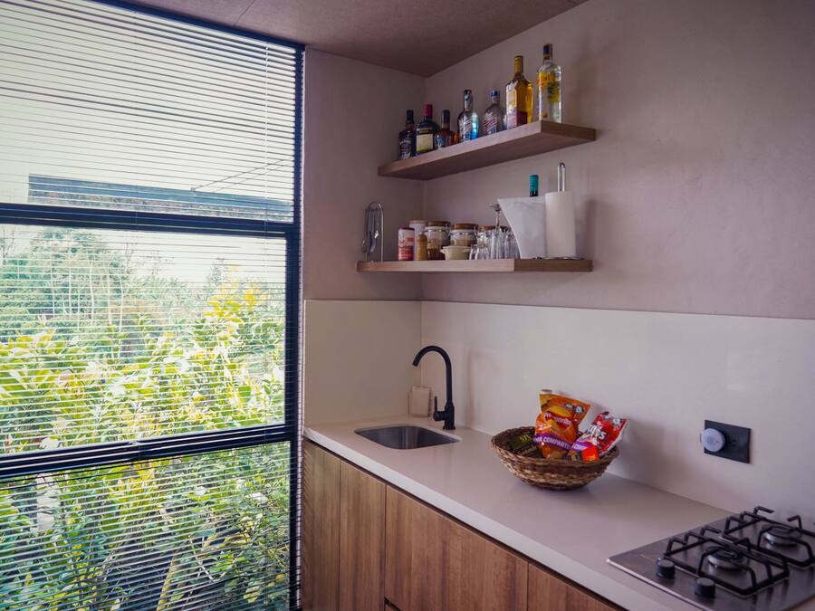 Una cocina con ventana, un lavamanos, una estufa a gas y repisas con botellas y frascos.