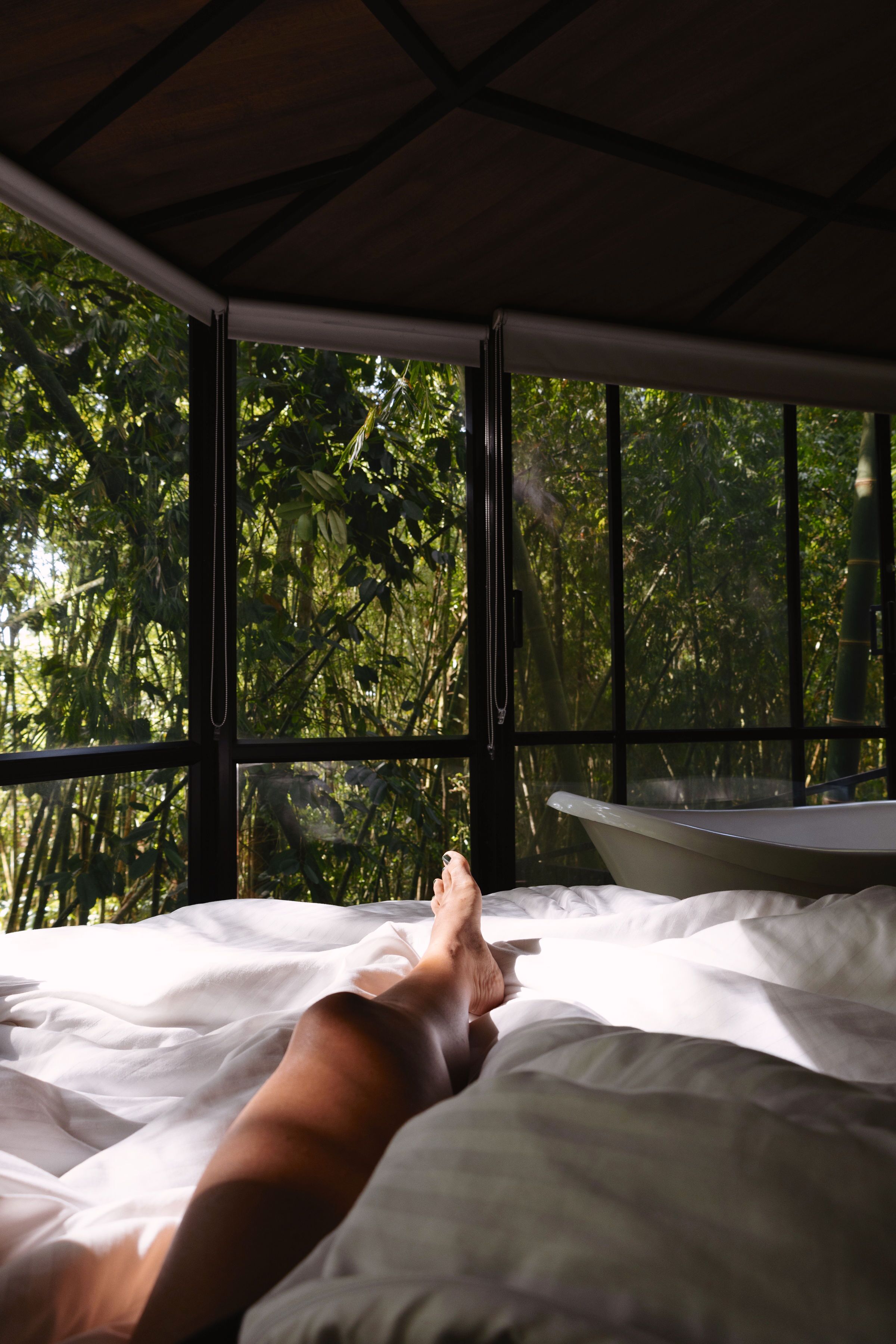 A bed with white bedding and a view of a bathtub through a window.