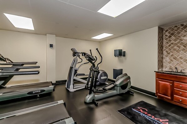 A gym with cardio machines, a weight bench, and a mirror.
