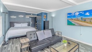 Un dormitorio moderno con cama, sofá de cuero negro, mesa de centro de vidrio y una pintura de un paisaje urbano en la pared.