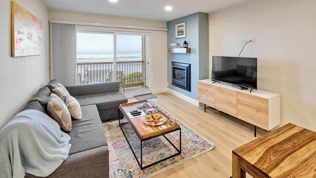 Een woonkamer met een bank, salontafel, televisie, open haard en een balkon met uitzicht.