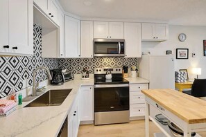 A modern kitchen with white cabinets, a microwave, a kettle, and a stove.