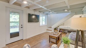 Uma sala de estar espaçosa com piso de madeira, escada, TV de tela plana e um canto de estar acolhedor com abajur e planta.