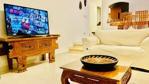 Een woonkamer met een houten salontafel, een witte bank en een televisie waarop een Netflix-interface wordt weergegeven.