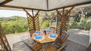 Een houten terras met een tafel voor vier personen, omringd door stoelen, met uitzicht op een weelderige tuin.