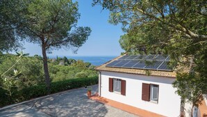 Een wit gebouw met een grindpad, zonnepanelen op het dak en uitzicht op zee.