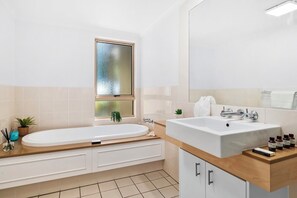 Bathroom features a large oval-shaped bathtub, separate sink area, and a large mirror above the sink.