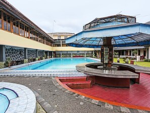 Una piscina con un deck circundante, una zona de estar cubierta y una pequeña fuente.