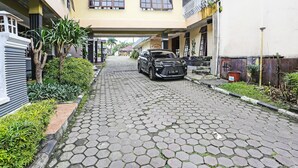 A paved street with a parked car, buildings with balconies, and greenery along the sides. - OYO 92088 171 Inn (Bogor)