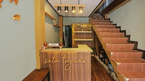 A reception desk with a wooden finish and the name "Satu Tjunan" displayed. A staircase with red tiles leads to a wooden platform. - OYO 92088 171 Inn (Bogor)